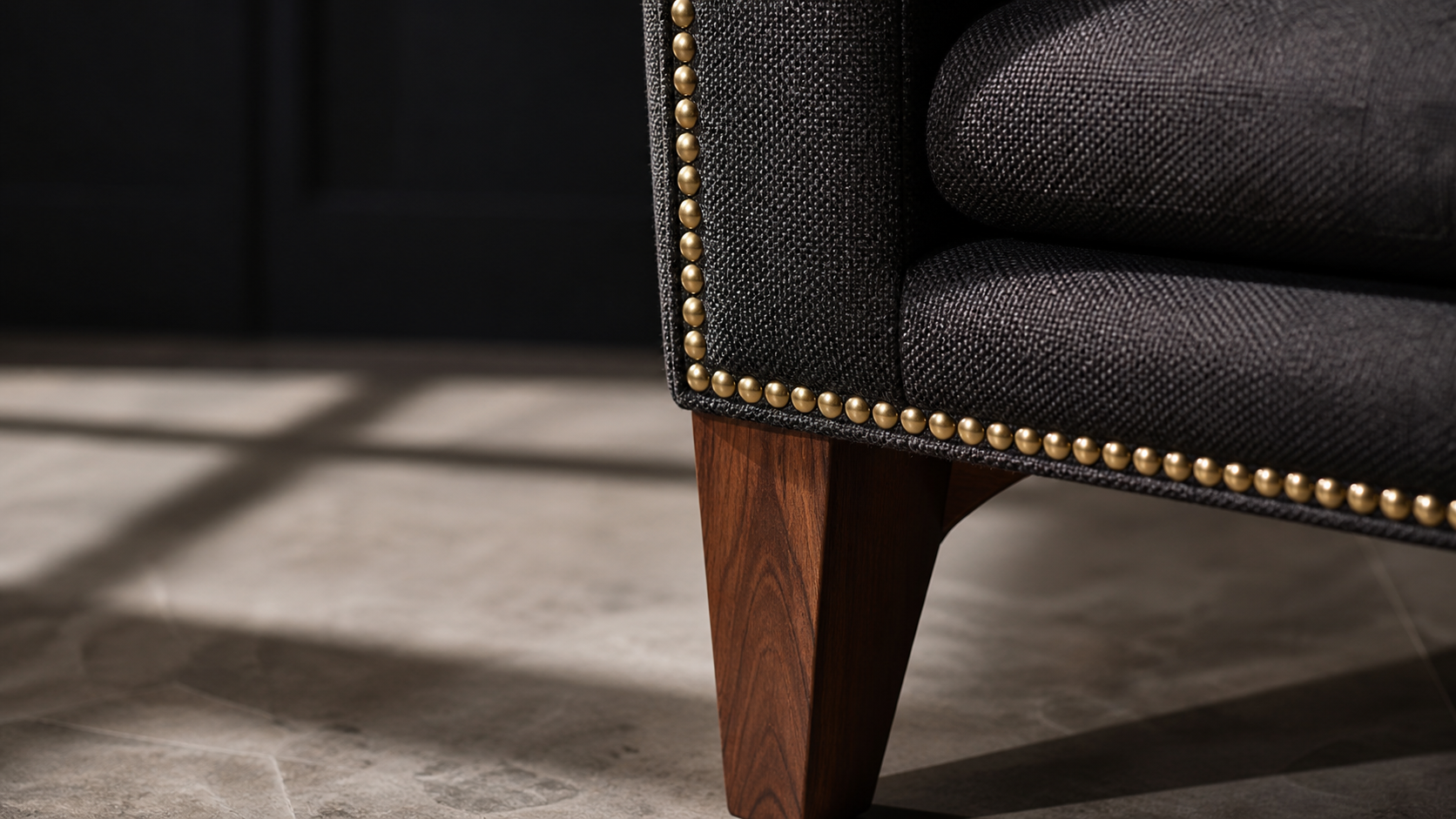 Close-up detail of contract-grade upholstered lobby chair showing fabric texture, brass nail head trim, and solid hardwood leg